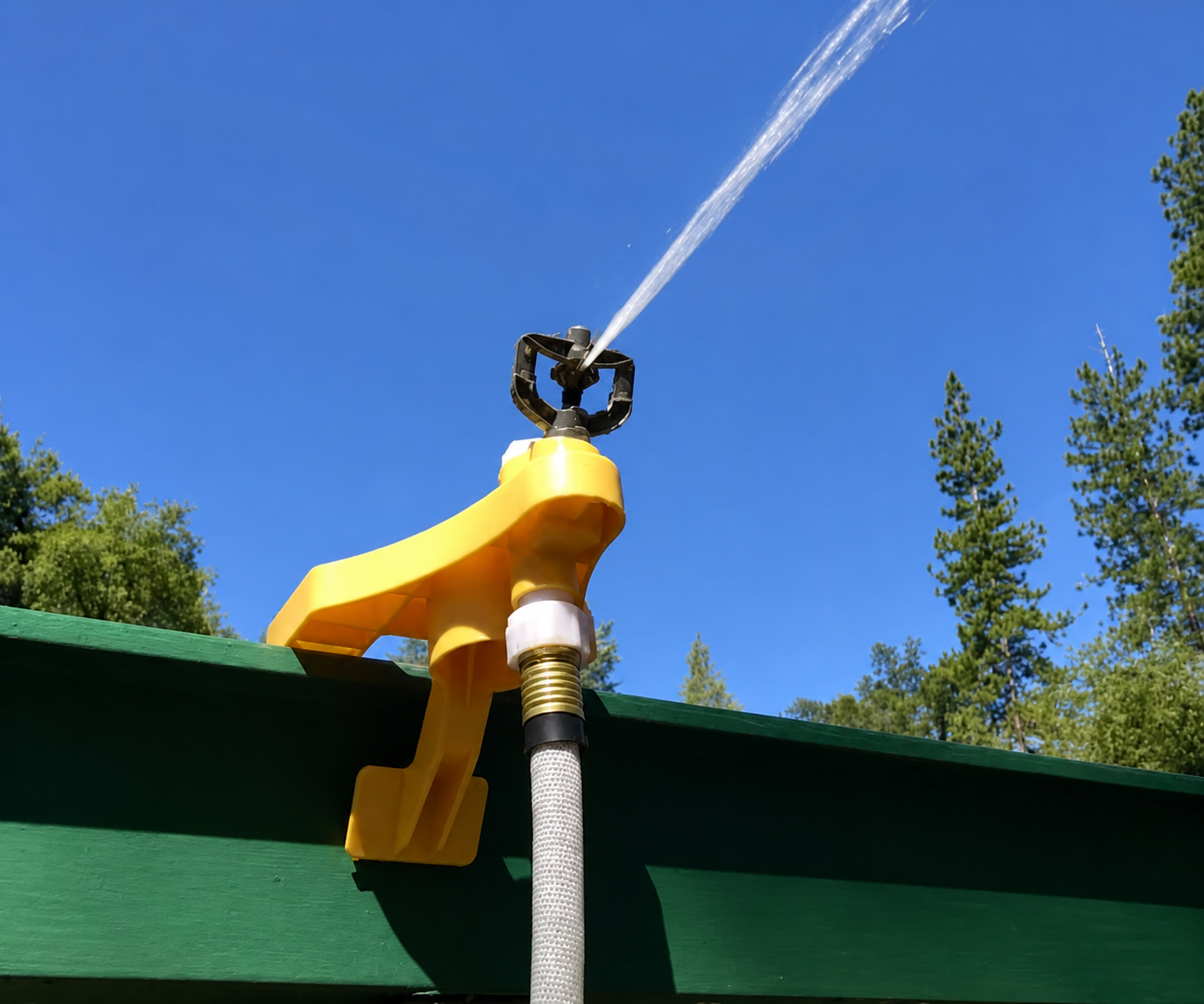 Yellow plastic gutter-clip sprinkler running on a green fascia board